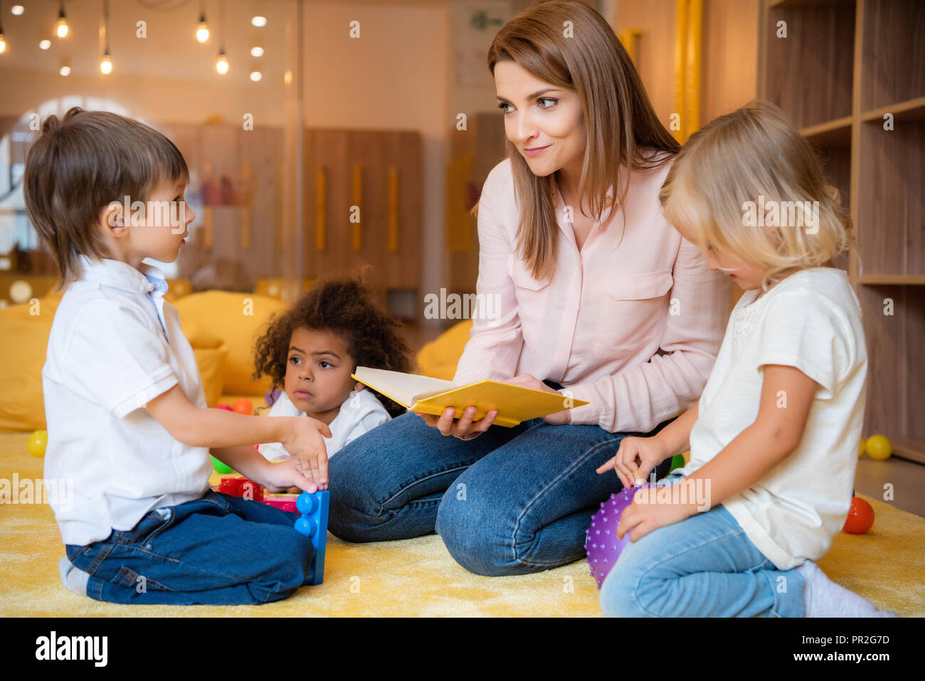 Erzieher lesen Buch für multikulturelle Kinder im Kindergarten Stockfoto