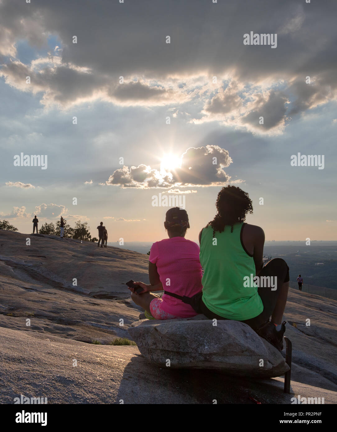 Nicht identifizierbare Wanderer beobachten die Sonne beginnt auf einem Felsen an der Spitze von Stone Mountain in Georgia an einem hellen Sommertag zu setzen Stockfoto