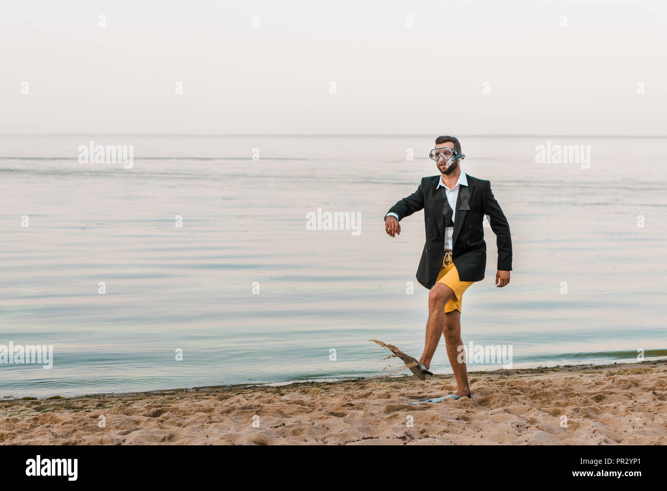 Mann in Schwarz Jacke und Hosen zu Fuß mit Maske und Flossen auf Meer Stockfoto