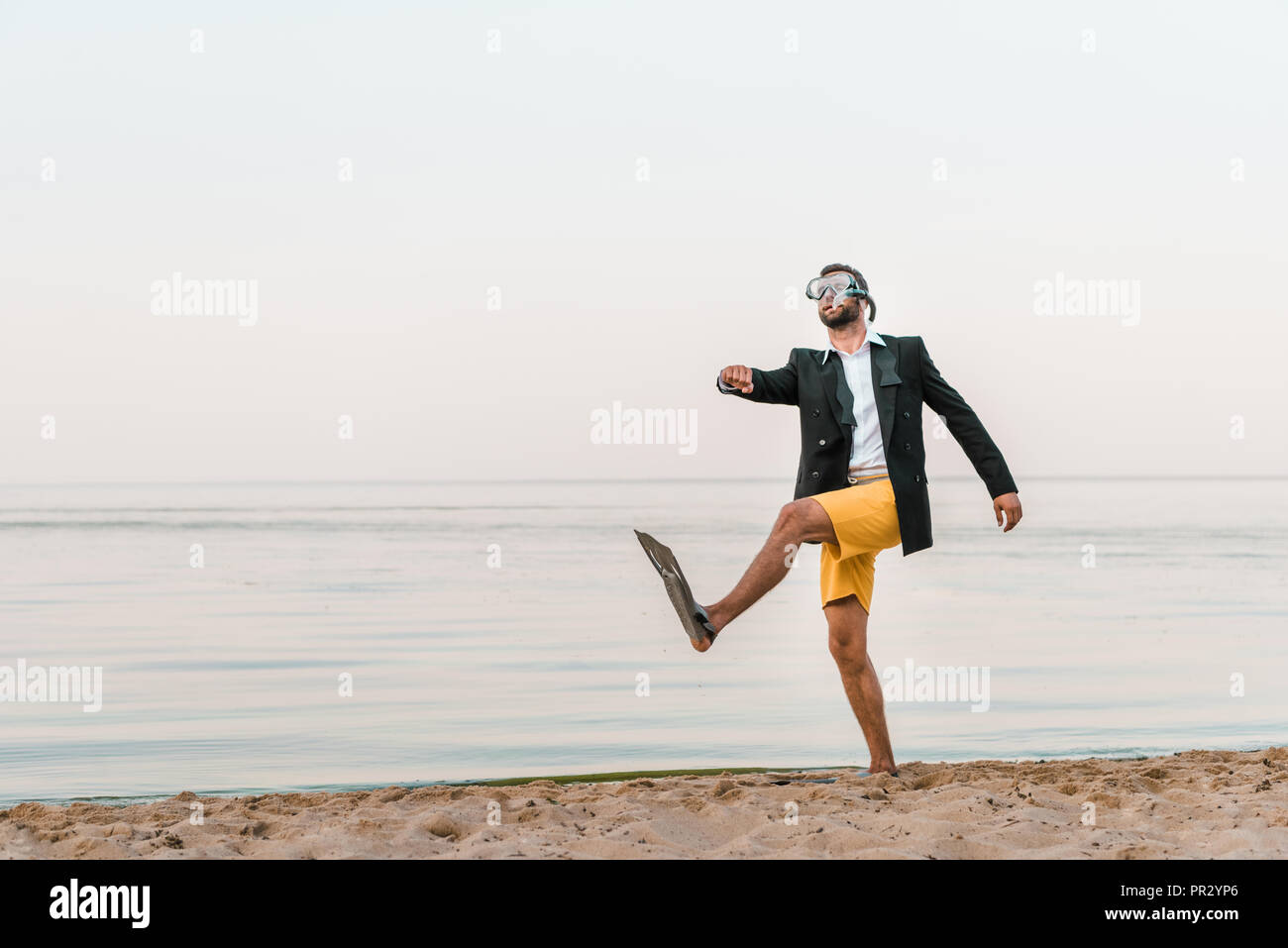 Mann in Schwarz Jacke und Hosen zu Fuß mit Maske und Flossen am Sandstrand Stockfoto