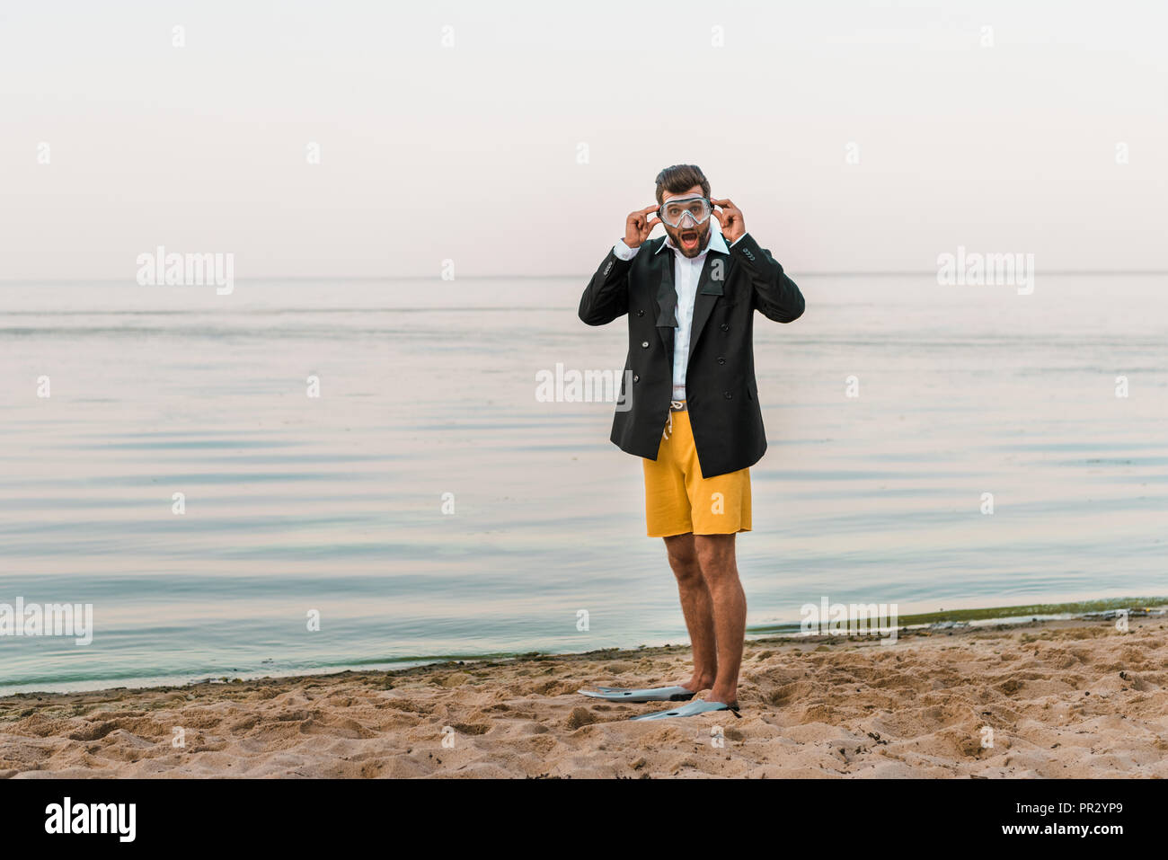 Schockiert, Mann in Schwarz Jacke, Hose und Flossen Maske tragen, Schwimmen am Strand Stockfoto