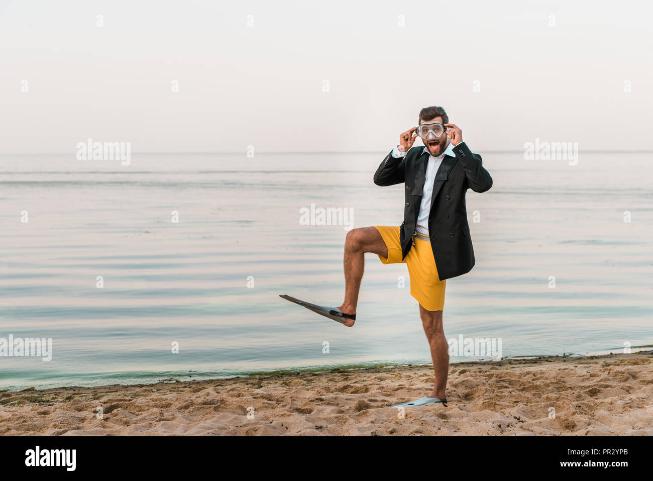 Überrascht Mann in Schwarz Jacke, Hose und Flossen Maske berühren, Schwimmen am Strand in der Nähe von Meer Stockfoto