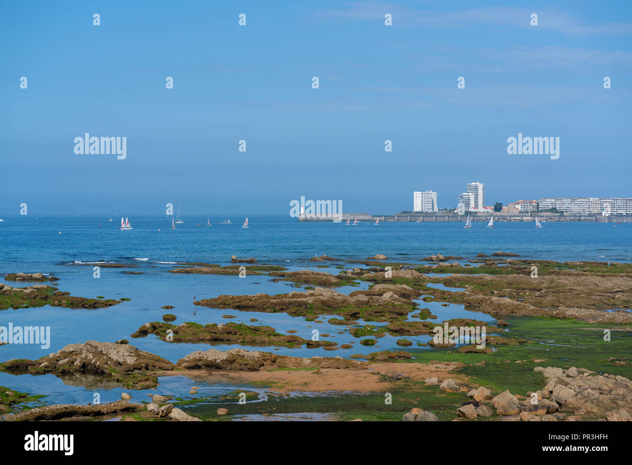 Leuchtturm auf Bootssteg mit Segelboot und Felsen in Les Sables d'Olonne in Vendee Frankreich Stockfoto