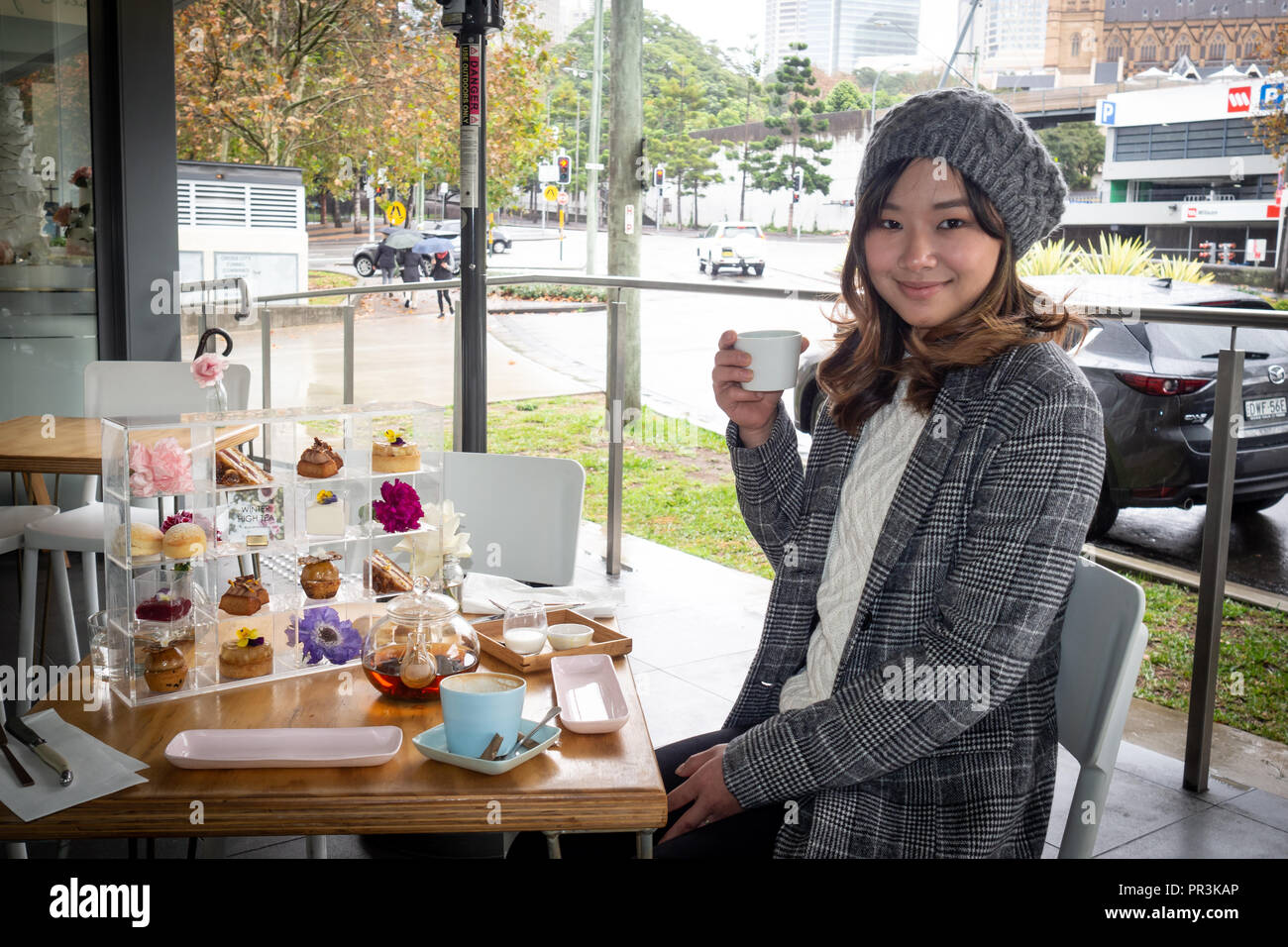 Junge Frau fröhlich draußen sitzen mit Kuchen und Tee Stockfoto