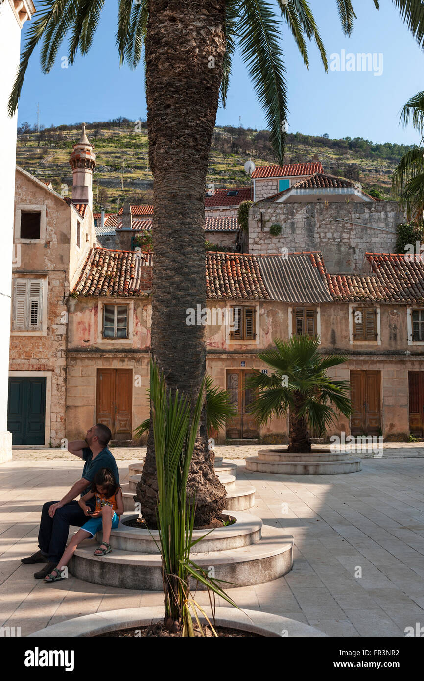 Vater und Tochter sitzen unter Palmen im ruhigen Platz Trg 30. svibnja 1992, gegenüber der Stadt, Kroatien Stockfoto