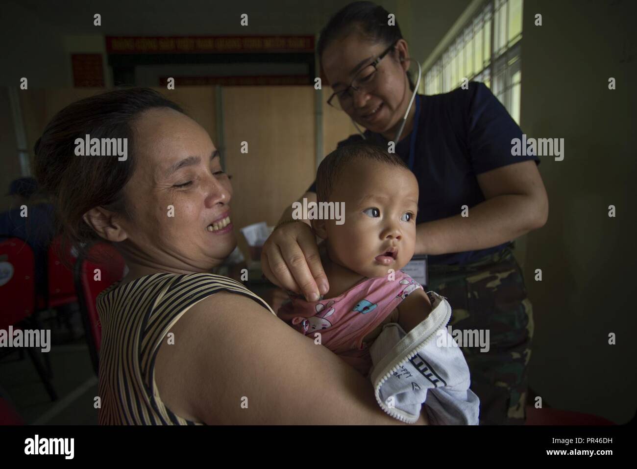 Dinh Thi Hong Nhi hält ihre Tochter als Königliche Laos Luftwaffe Oberstleutnant Phonesouk Soukleuangkham prüft die Atmung des Babys an einem Gesundheit Service Öffentlichkeitsarbeit Veranstaltung während der Pacific Engel (PACANGEL) 18-2 im Kulturzentrum Haus der Tam Giang Gemeinde im Nui Thanh, Quang Nam Provinz, Vietnam, Sept. 10, 2018. Das Gesundheitswesen outreach site allgemeine Medizin, Physikalische Therapie, Optometrie und zahnmedizinische Kliniken, in denen mehr als 600 Teilnehmer erwartet werden, durch die tägliche, bis die Operation beendet Sept. 15. Bemühungen während der PAC ENGEL durchgeführt, um die USA und Partner Nationen verbessern und bauen relationsh Stockfoto