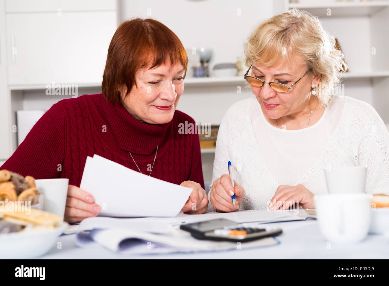 Freundliche ältere Frauen am Küchentisch sitzen Arbeiten mit Dokumenten Stockfoto