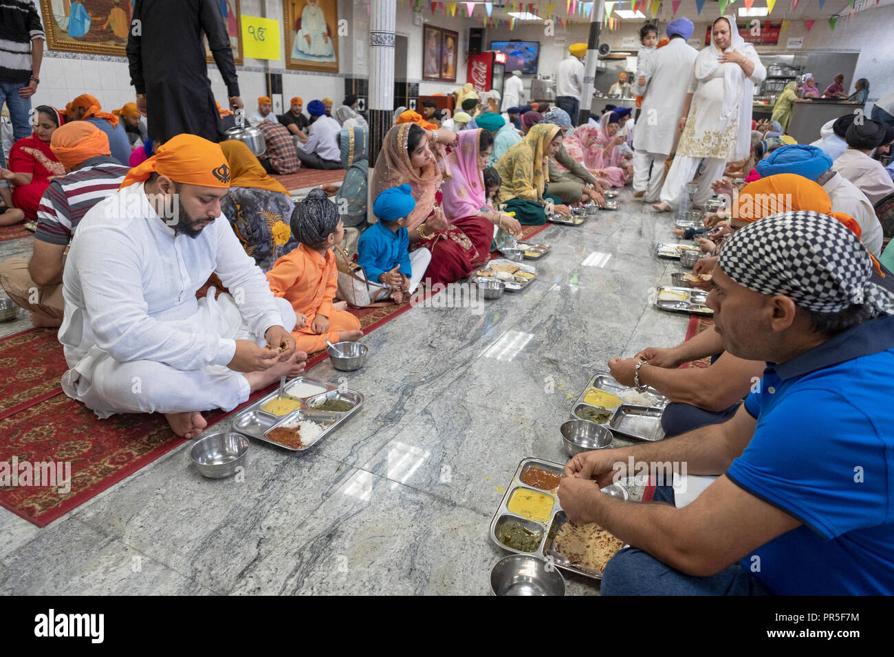 Frau, Mann und Kinder essen in einem Sikh-tempel langar, einem Raum, wo keine Gäste vegtarian Essen serviert werden. Stockfoto