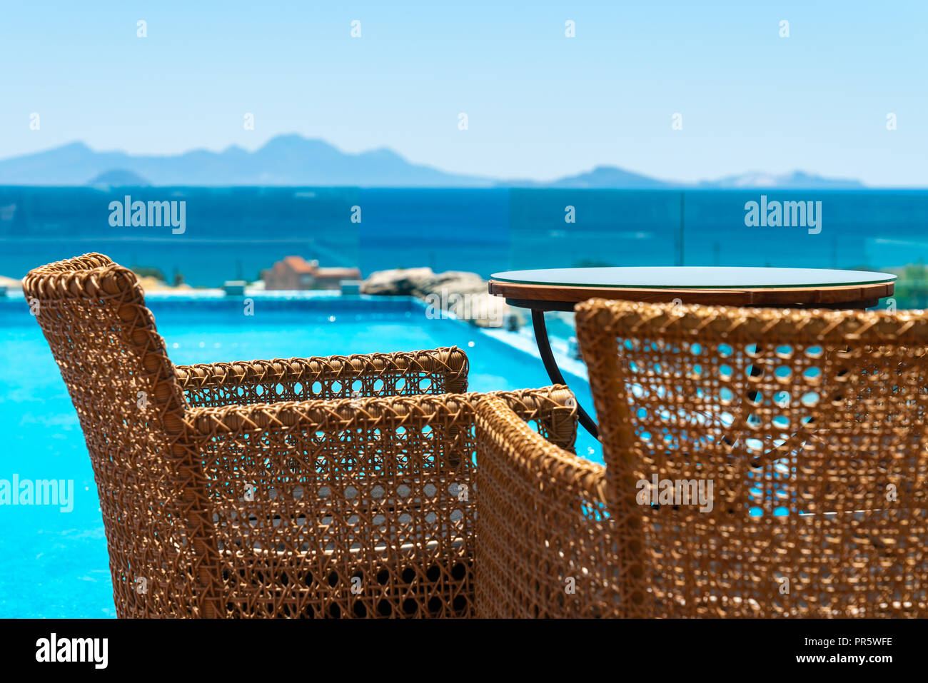 Blick über ein Schwimmbad mit Korb Tisch und Stühle im Vordergrund und Berge im Hintergrund Stockfoto