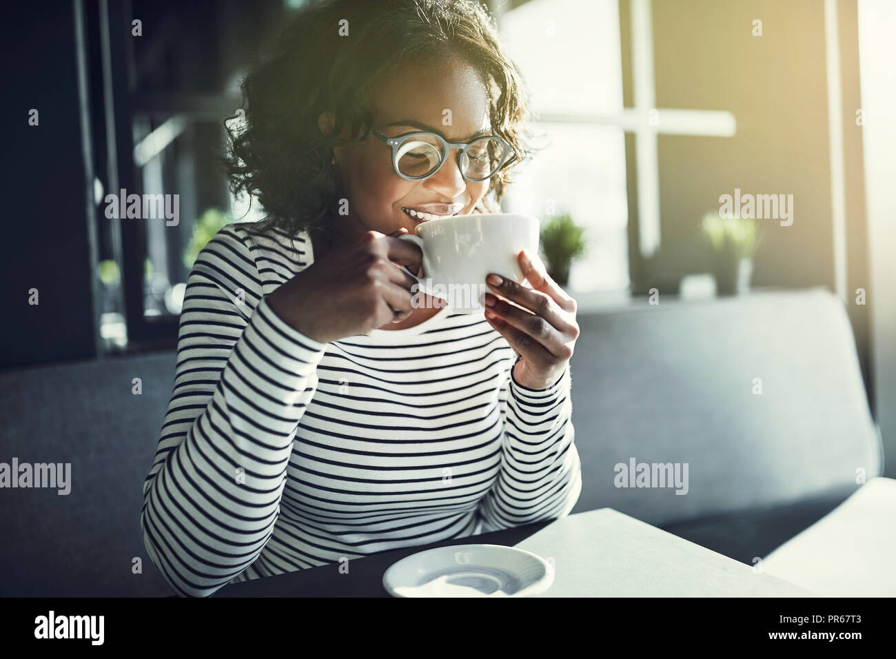Lächelnden jungen afrikanischen lächelnde Frau mit geschlossenen Augen das Aroma ihrer Tasse Kaffee genießen, während in einem Cafe sitzen Stockfoto