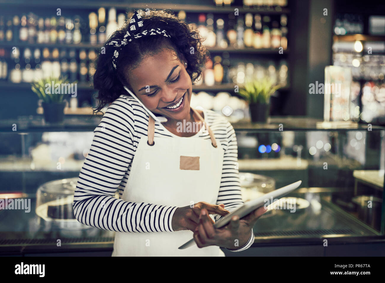 Lächelnden jungen afrikanischen Unternehmer stehen in Ihrem Cafe Reservierungen auf einem Handy und die Verwendung eines Tablet Stockfoto