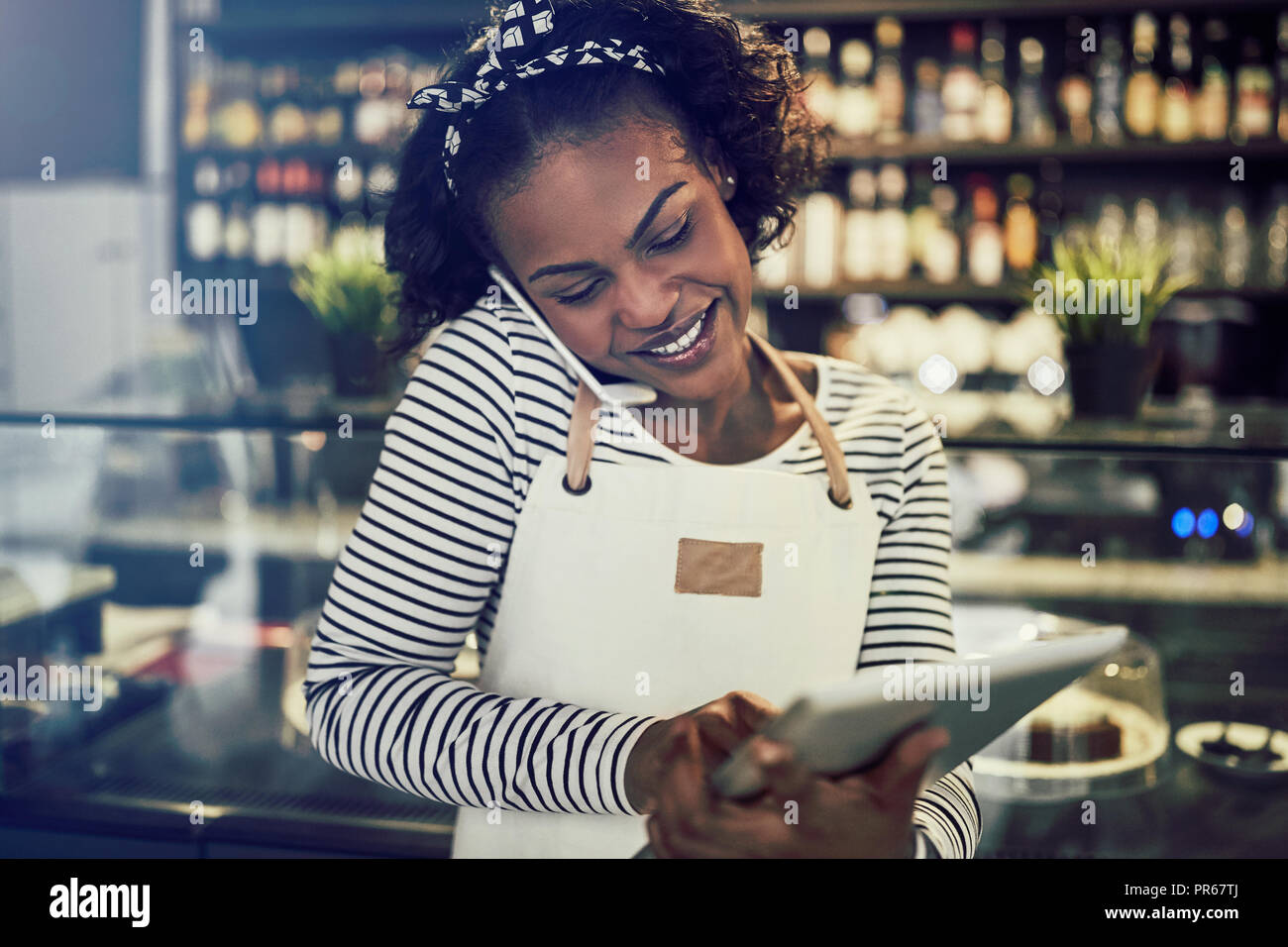 Lächelnden jungen afrikanischen cafe Inhaber Reservierungen über das Telefon und über einen digitalen Tablet Stockfoto