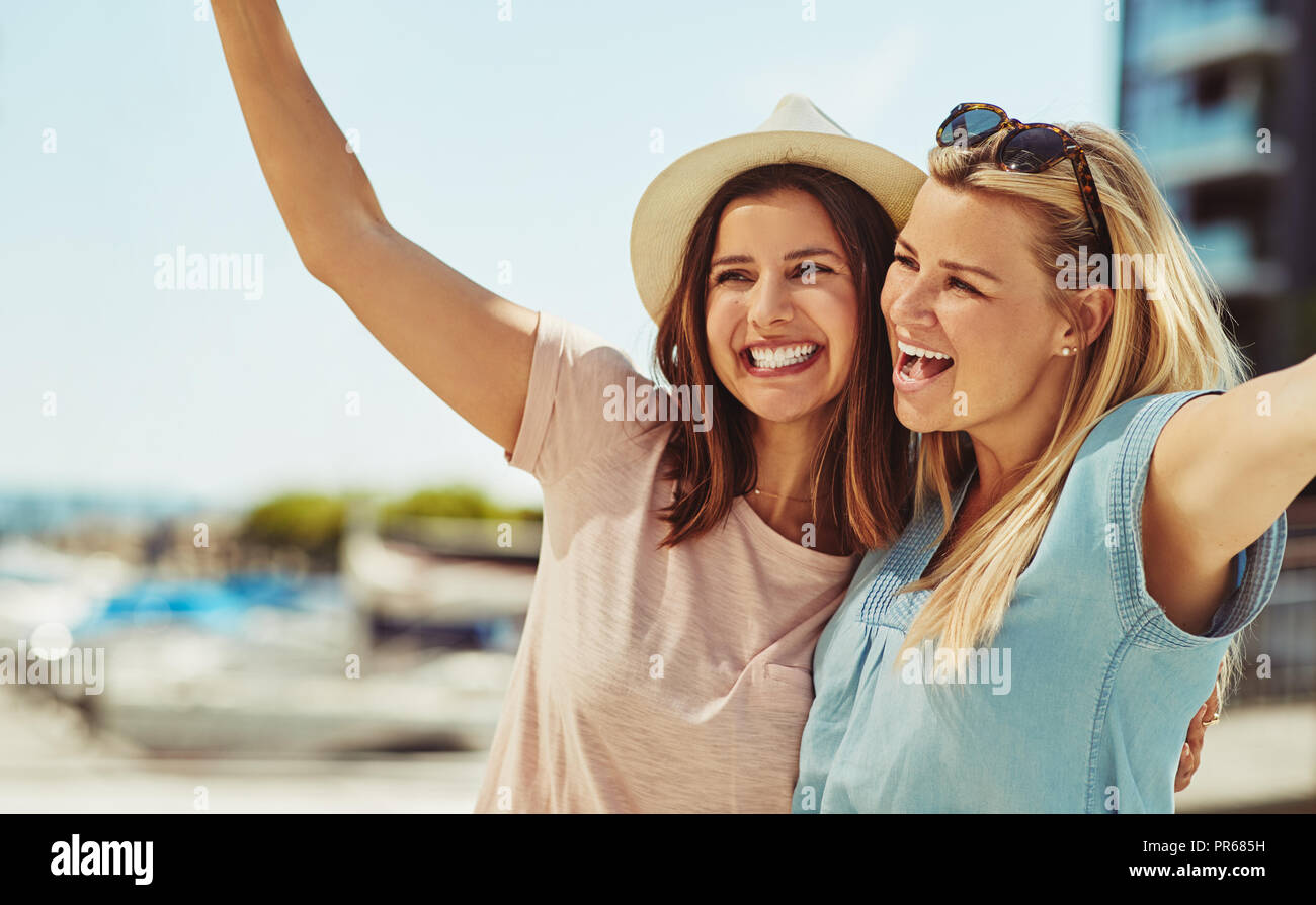 Zwei unbeschwerte Junge weibliche Freunde lachen beim stehen Arm in Arm zusammen in der Stadt im Sommer Stockfoto