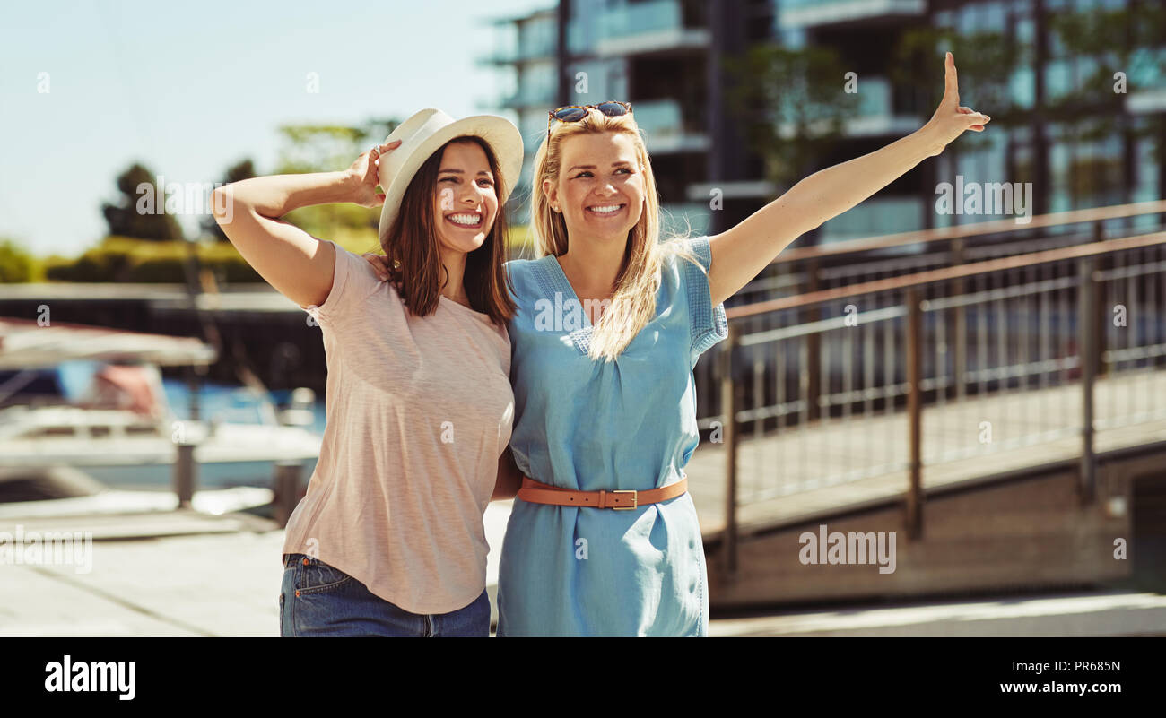 Zwei unbeschwerte Junge weibliche Freunde lachen und Spaß beim Gehen Arm in Arm zusammen in der Stadt im Sommer Stockfoto