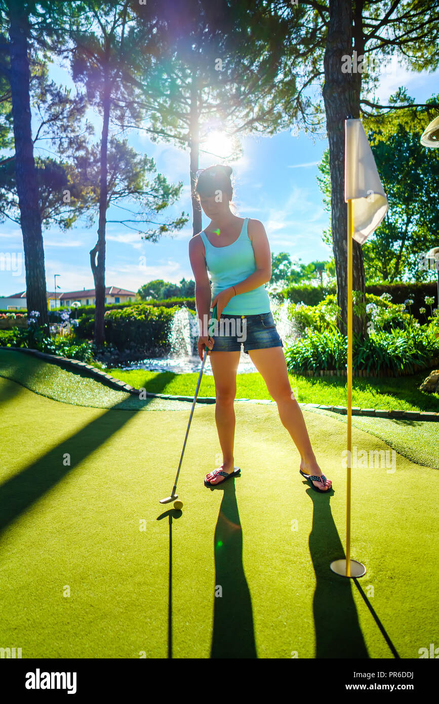 Mini Golf - Frau Golf spielen auf grünem Gras bei Sonnenuntergang Stockfoto