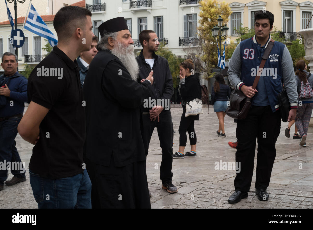 Ein orthodoxer Priester spricht zu einer Gruppe von Menschen in den Straßen von Athen, Griechenland Stockfoto