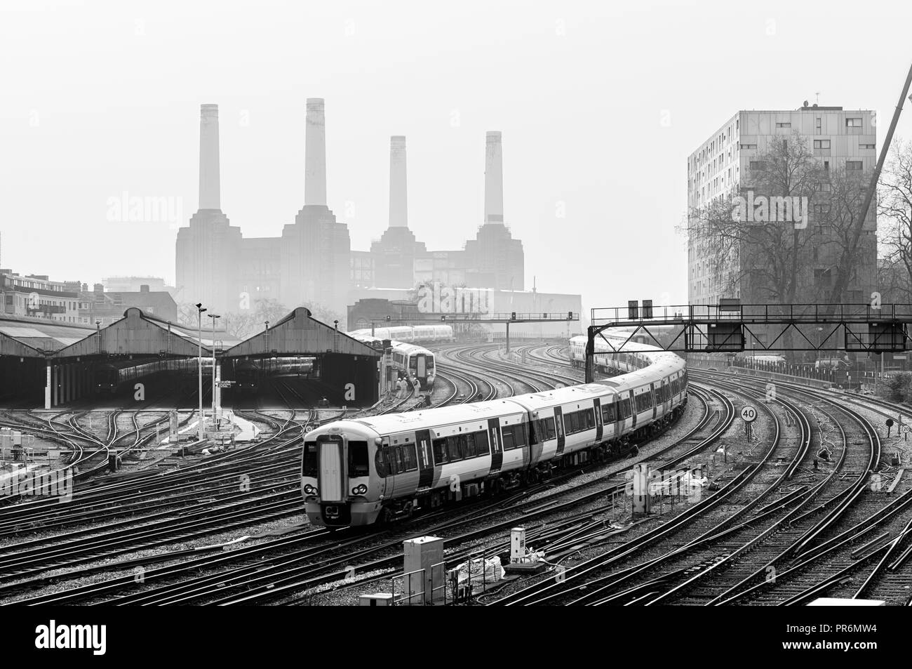 Bewegen Nahverkehrszüge und Bahnstrecken in London, mit Battersea Power Station hinter dem Nebel im Hintergrund erkannt zu werden. Schwarz und Weiß. Stockfoto