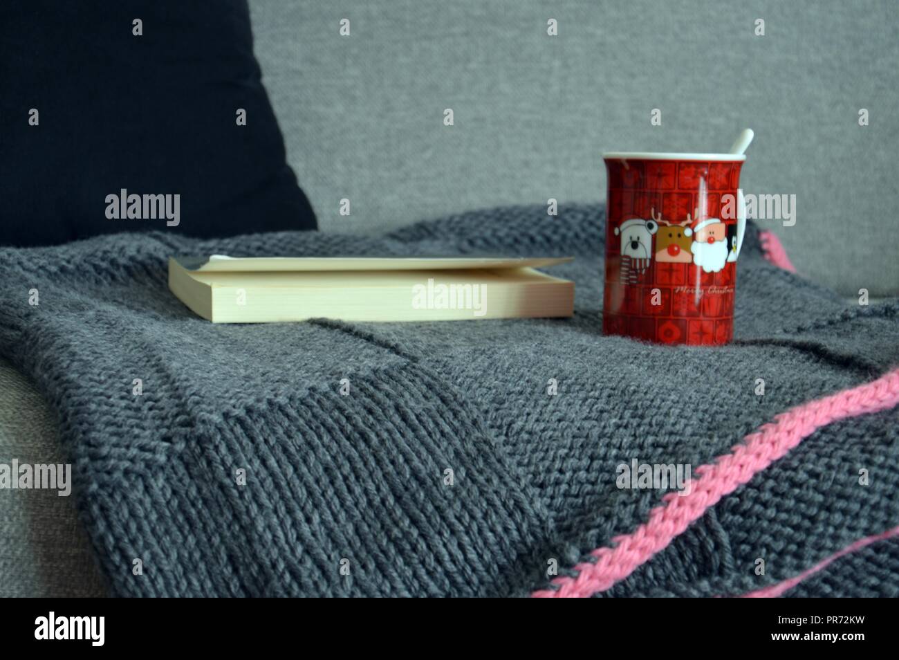 Winter Entspannung: Ein gutes Buch und einer Wolldecke auf dem Sofa mit einer heißen Tasse Kaffee Stockfoto