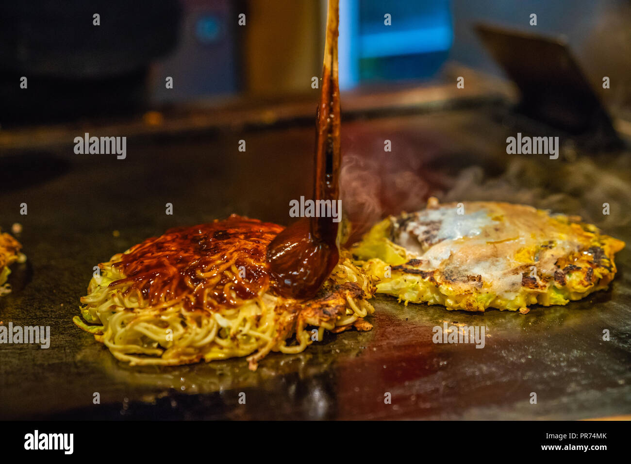 Chef kocht traditionelle japanische Lebensmittel genannt, Okonomiyaki, er fügt pikanter Sauce in der Nahrung Stockfoto