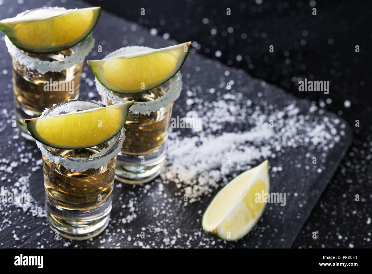 Schwarzer Hintergrund mit Tequila Gläser verstreut mit Salz und Limette. Alkoholfreien Cocktail. Mexikanische traditionelle Getränk Stockfoto