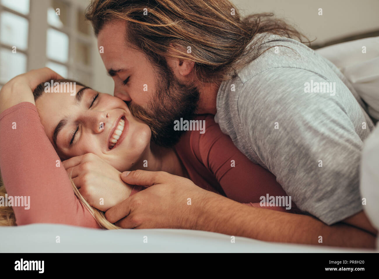 Paar im Bett verbringen die Zeit zusammen mit dem Menschen und seinem Partner. Lächelnde Frau mit geschlossenen Augen, küsste und ihren Mann liebte. Stockfoto