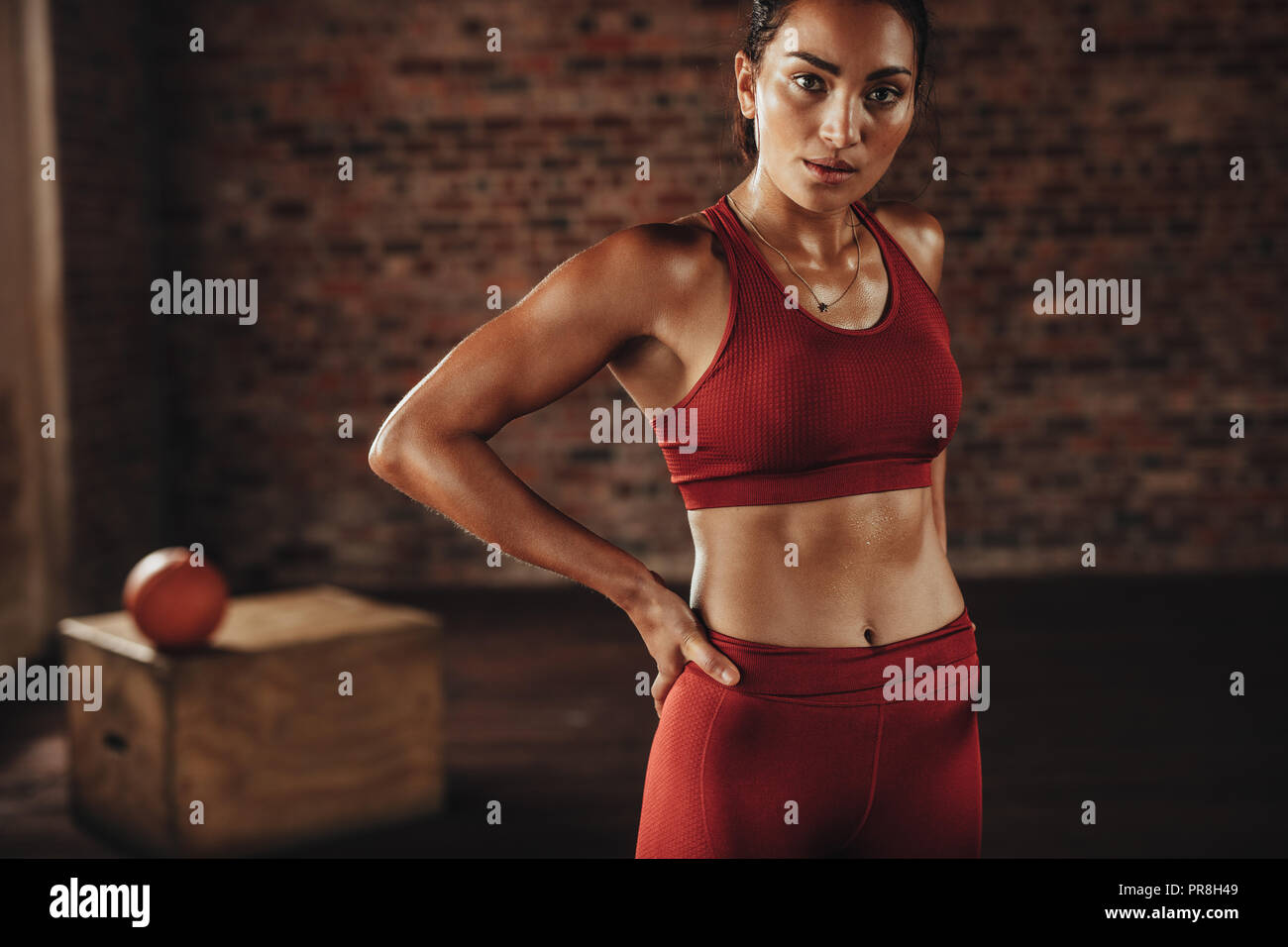 Frau, die nach dem Training im Fitnessstudio steht. Gym-Frau in roter Sportkleidung, die in die Kamera schaut. Stockfoto