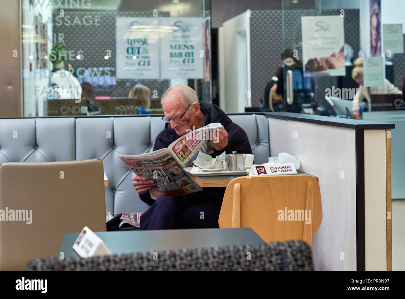 Ältere Menschen lesen die Sonne Zeitung in einem Cafe im Einkaufszentrum in Guildford, Surrey Stockfoto