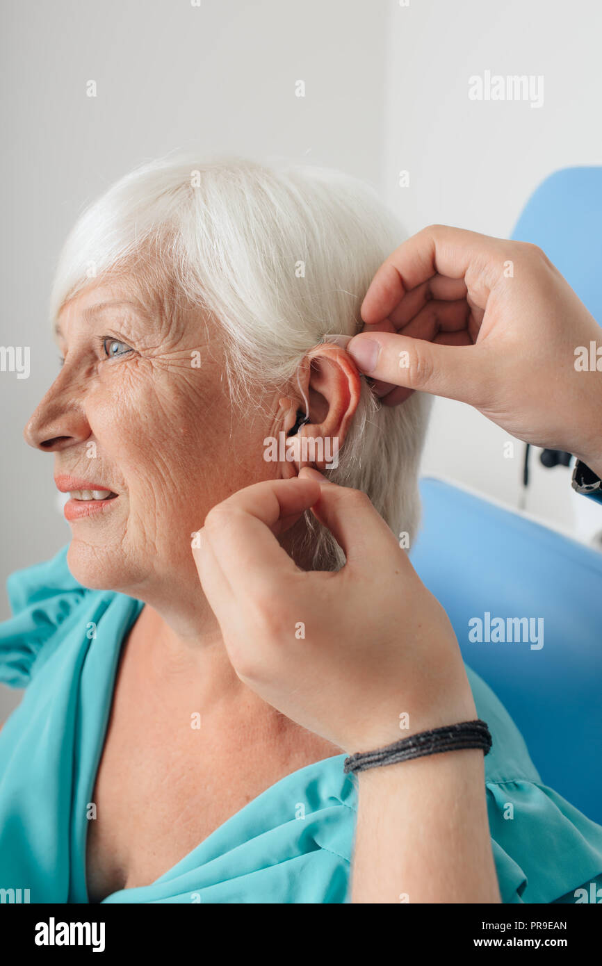 Doctor's Hand Anwendung von Hörgeräten für gealterte Frau 7/8 Stockfoto