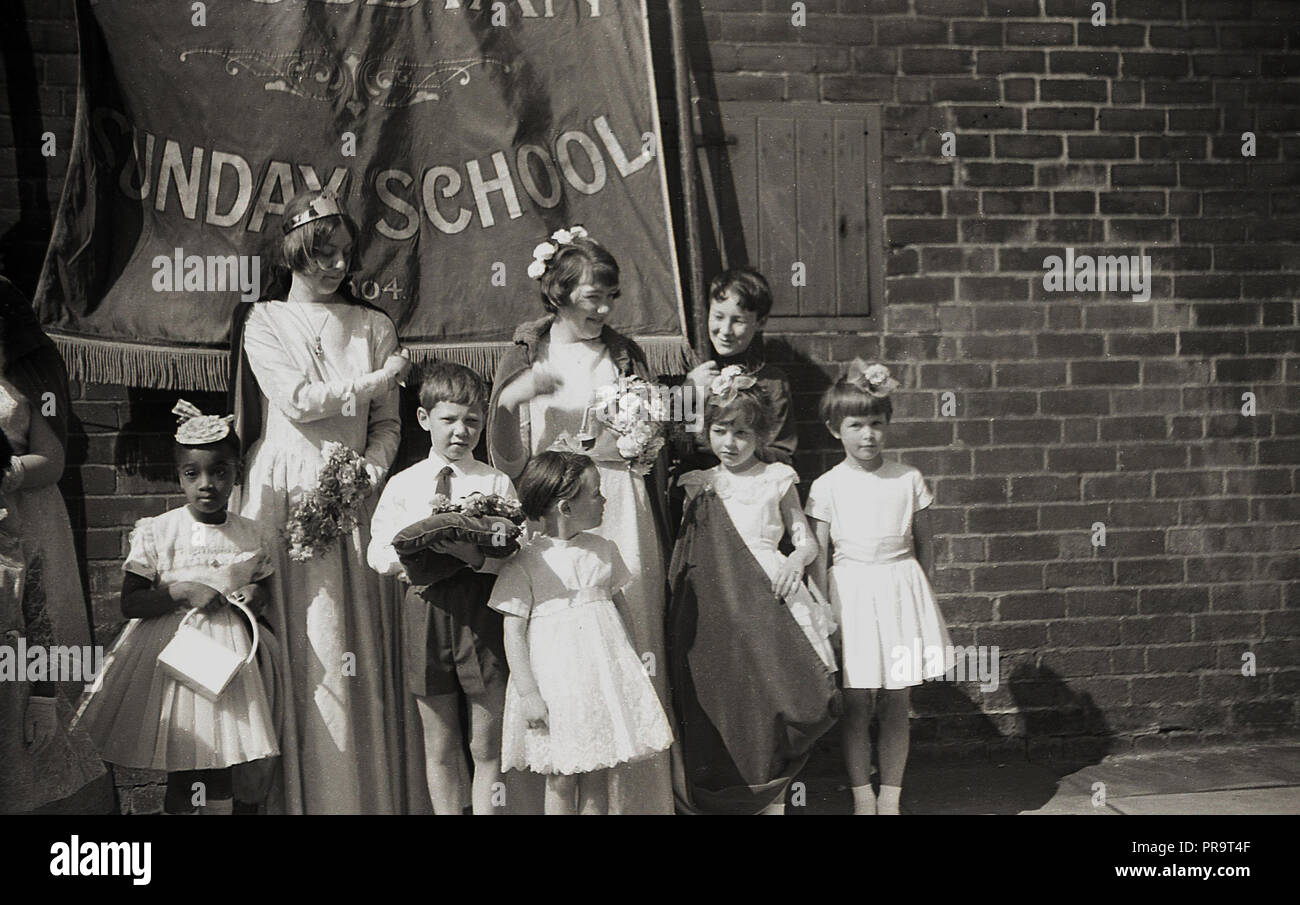 1950er Jahre, historische, Sheffield, junge Kinder und Mütter stehend außerhalb in einer Straße unter einer Fahne für die Wesleyan Methodist Church Sonntagsschule, vor der Teilnahme an einer Parade. Christlichen Charakter, eine Sonntagsschule war eine Bildungseinrichtung, zuerst in den 1780er Jahren in England gegründet, um eine Ausbildung zu Arbeiterklasse Kinder zur Verfügung zu stellen und besonders beliebt waren im nördlichen Englischen Städte wie Manchester und Sheffield. Die Lehre der Wesleyan Kirche, genannt für die Rechte der Frau und trat gegen Kinderarbeit. Stockfoto