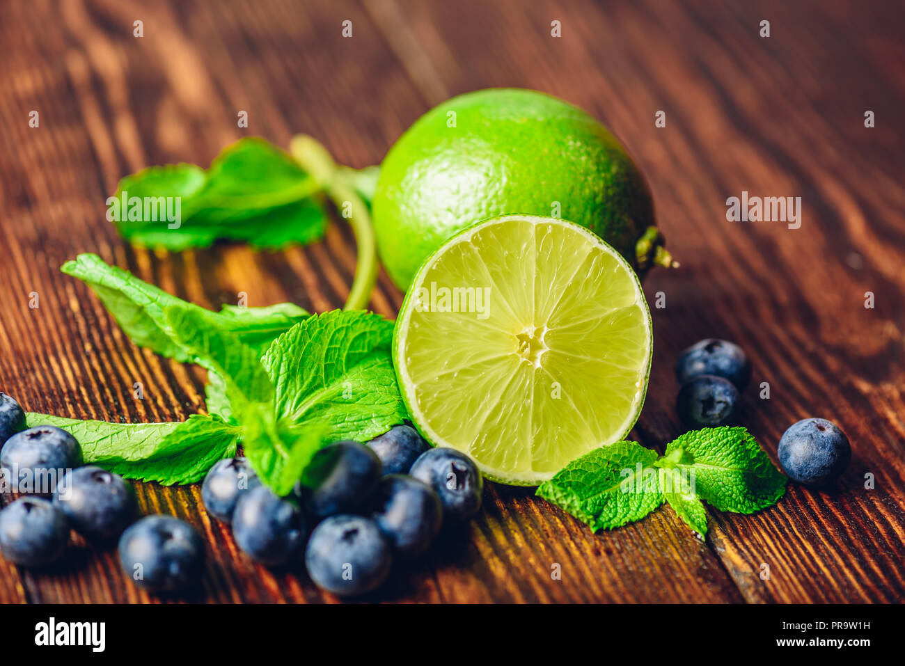 Frische Heidelbeeren, die Hälfte der Limette und Minze auf hölzernen Tisch. Zutaten für die Vorbereitung infundiert Wasser. Stockfoto