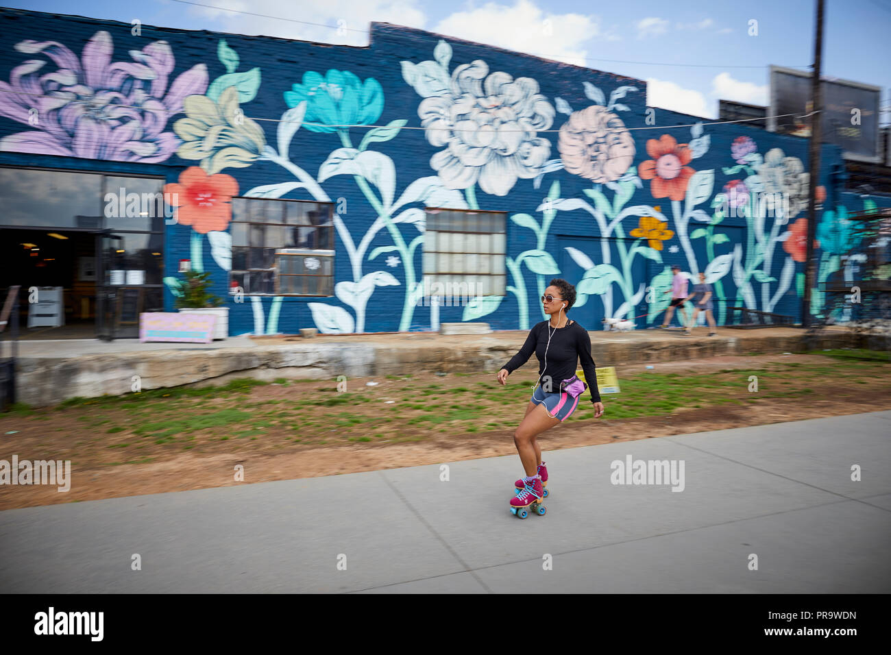 Atlanta, Hauptstadt des US-Bundesstaates Georgia, eine Frau rollerbladen oder Skaten auf einem Laufsteg mit einer hellen geblümten Wand im Hintergrund Stockfoto