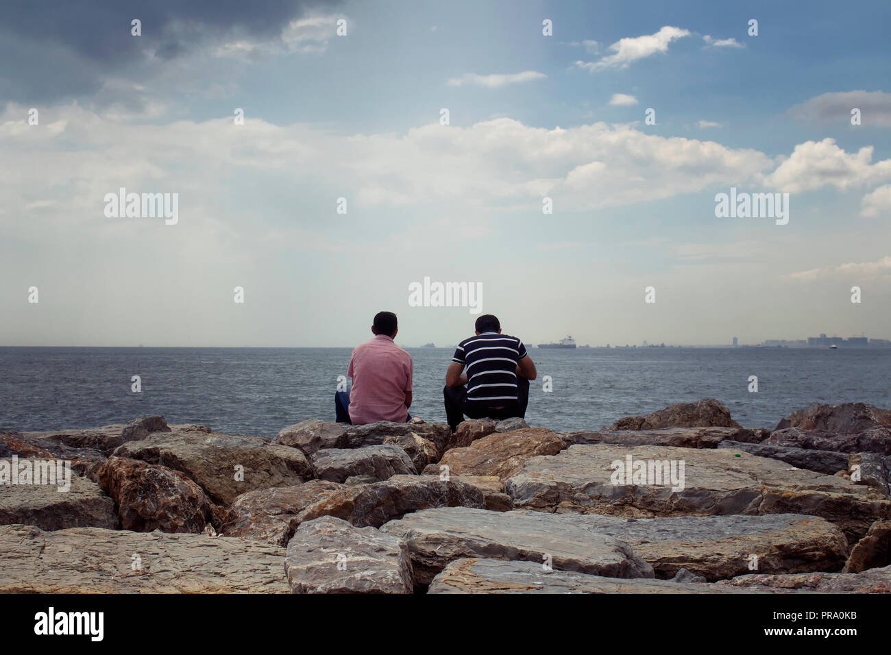 Aussicht auf zwei unkenntlich Männer sitzen auf den Felsen durch den Bosporus. Das Bild ist in der Gegend namens Moda befindet sich auf der asiatischen Seite von Istan erfasst Stockfoto