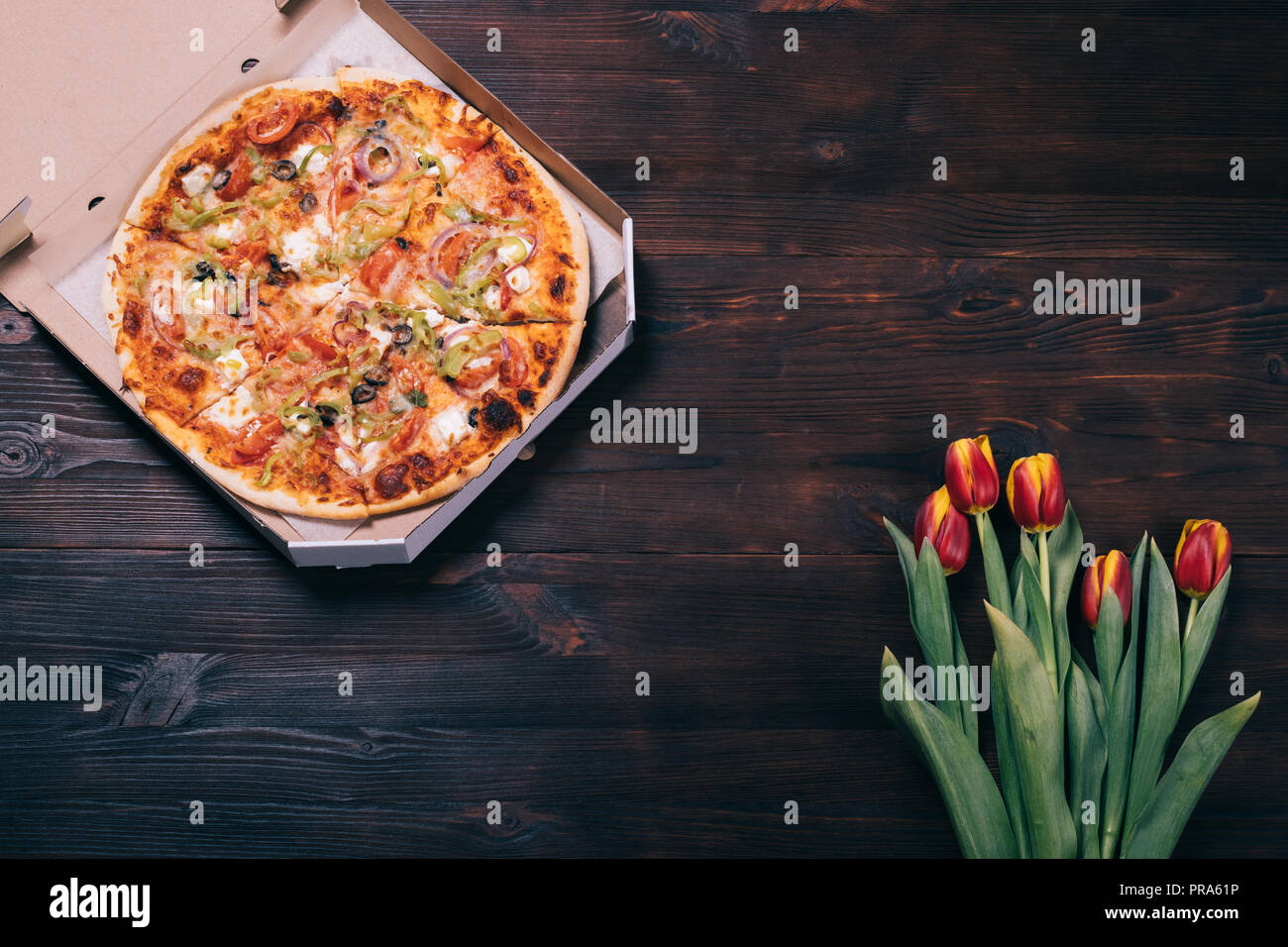 Runde Pizza Im Karton Auf Dunkelbraunen Holzernen Tisch In Der Nahe Von Bouquet Von Frischen Rot Gelben Blumen Tulpen Ansicht Von Oben Stockfotografie Alamy
