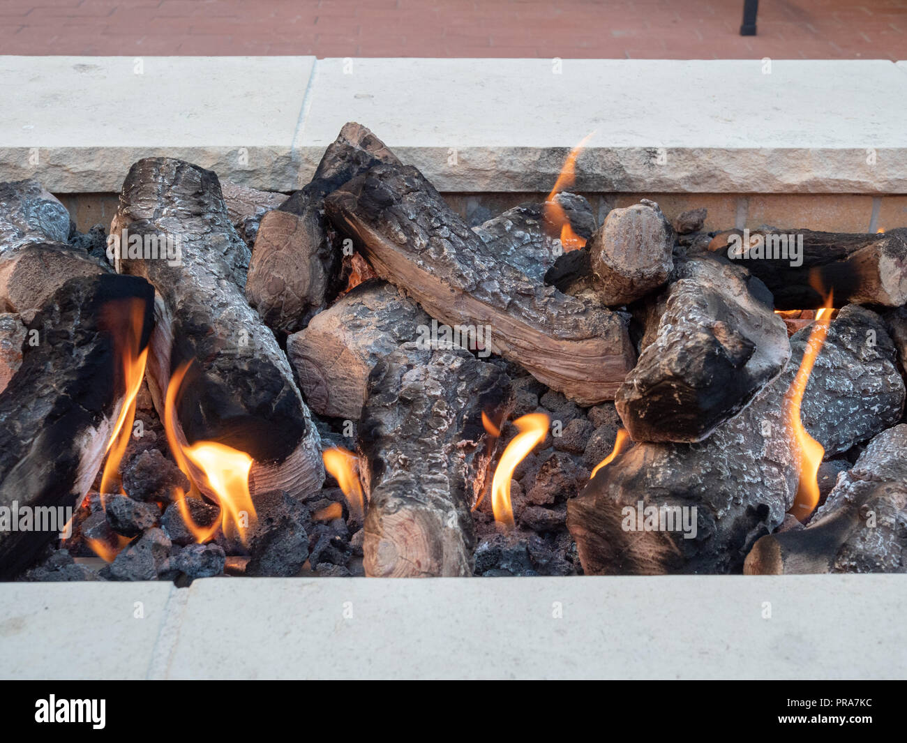 Logs im offenen Feuer sitzen in einem weißen Stein Feuerstelle Stockfoto