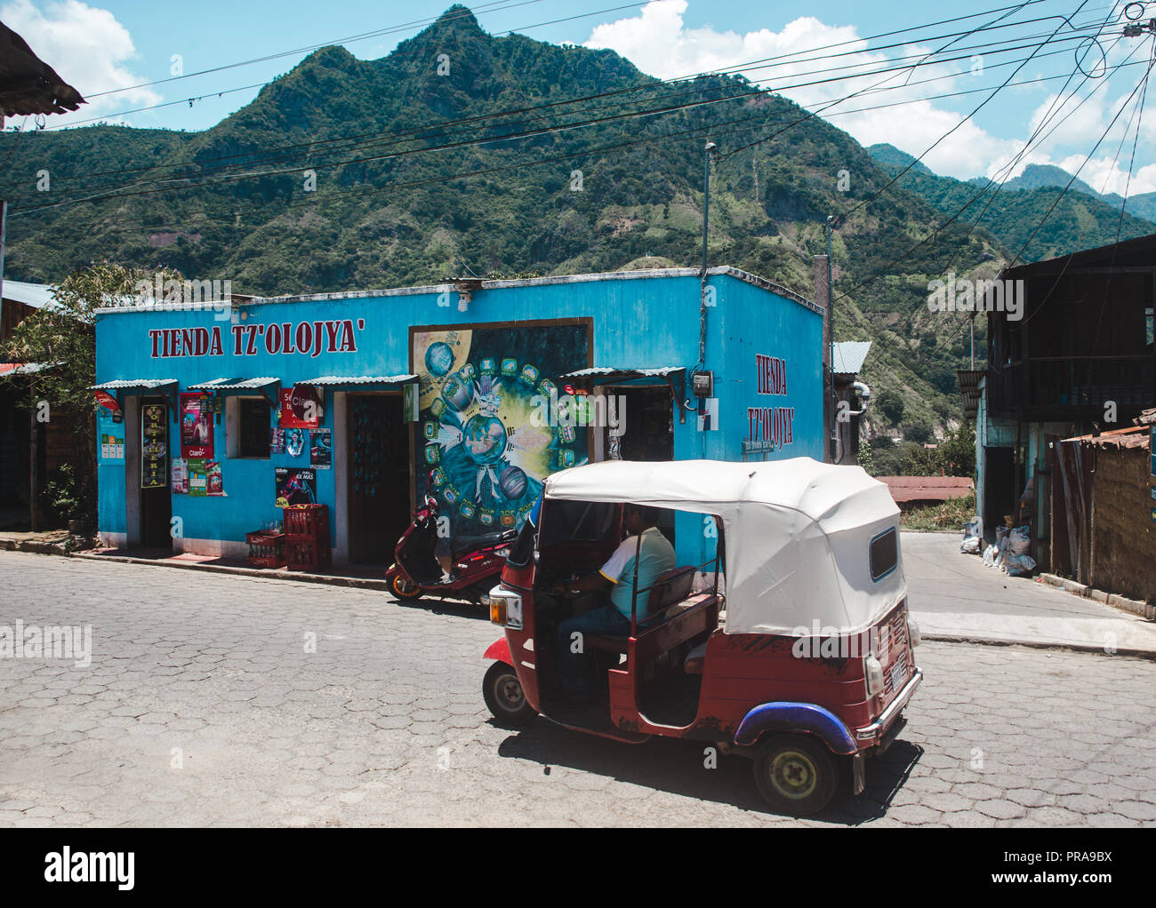 Motorisierte tuk tuk Antriebe eine kleine bunt bemalte "tienda 'Convenience Store in der kleinen Stadt San Juan, am Atitlán-See Stockfoto