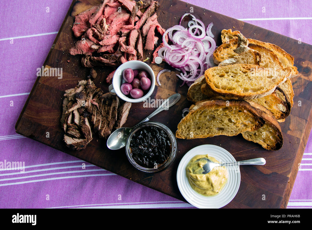 Roastbeef und Steak auf dem dunklen Board mit geröstetem Weißbrot, Oliven, in Scheiben geschnittene Zwiebeln, Senf und karamellisierten dunkle Zwiebel Sauce. Stockfoto