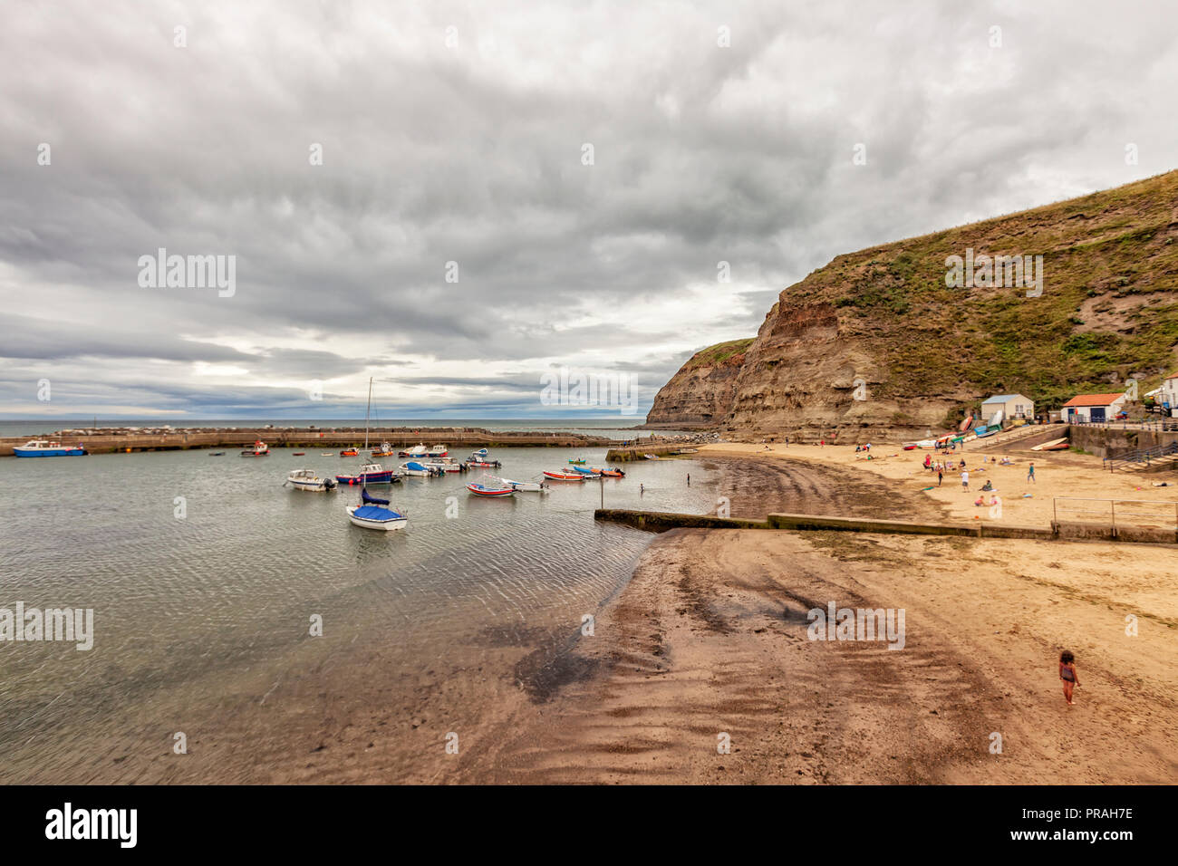 Staithes, North Yorkshire, England, 22. August 2018: Moody Himmel bei Sonnenuntergang über Wasser mit Fischerbooten am Strand Staithes verankert. Stockfoto