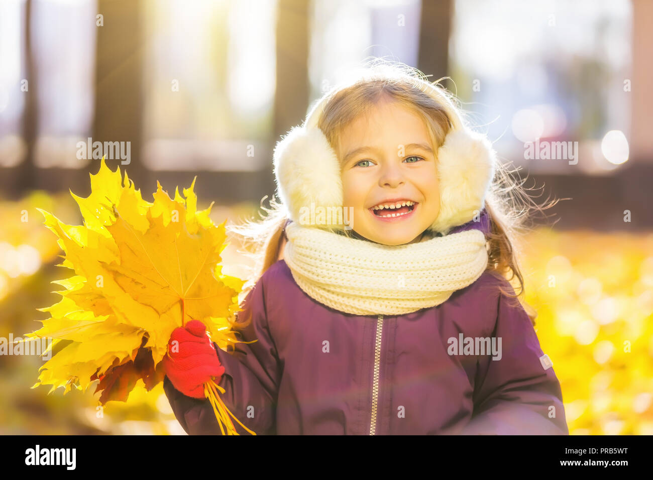 Glückliches kleine Mädchen in Ohrenklappen mit Herbst Blätter Stockfoto