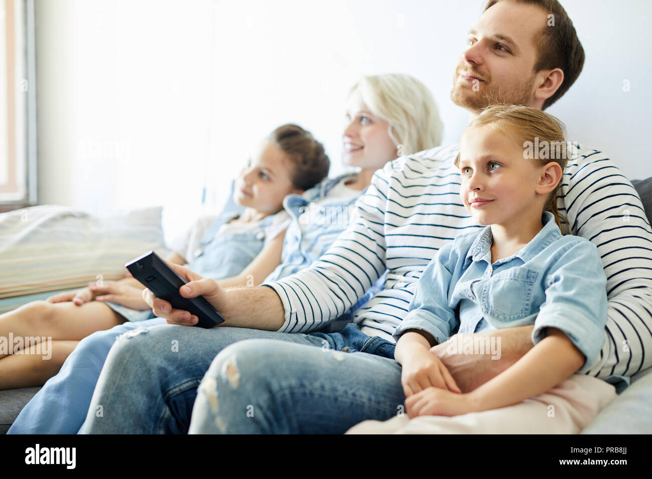 Junge Familie von Eltern und zwei kleinen Töchtern sitzen auf dem Sofa und Fernsehen Stockfoto