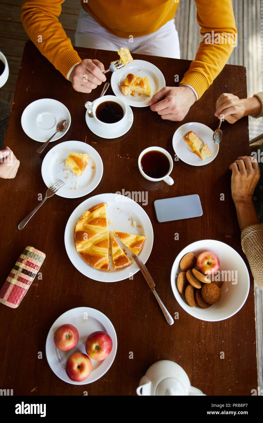 Hohe Betrachtungswinkel der unkenntlich senior Freunde an den hölzernen Tisch und trinken schwarzen Tee mit Kuchen, Kekse und Äpfel sitzen Stockfoto