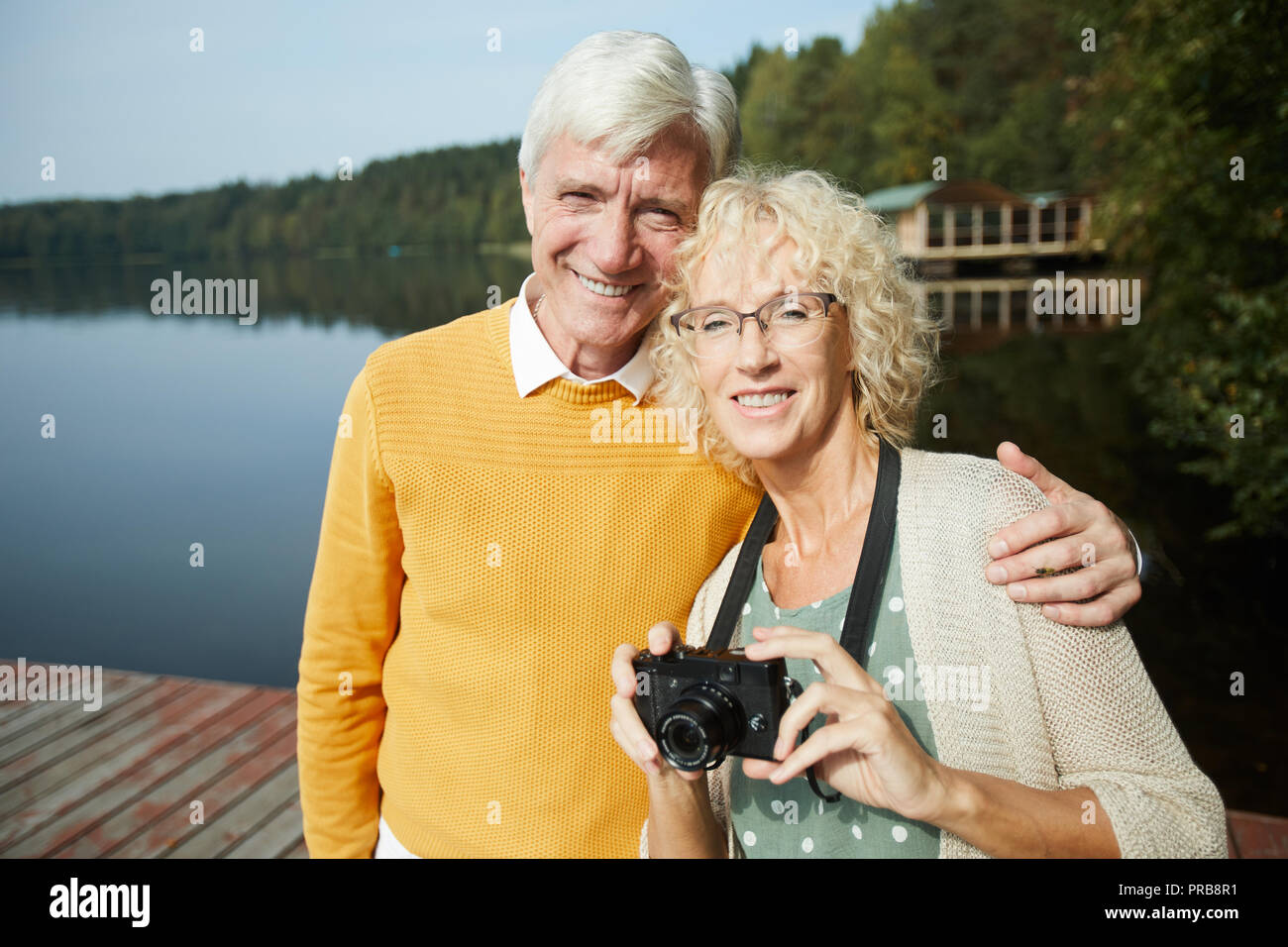 Gerne ältere Touristen in modische Kleidung umarmen und lächelnd an der Kamera beim Stehen auf Pier und Kamera, sie ruhen in Land Stockfoto