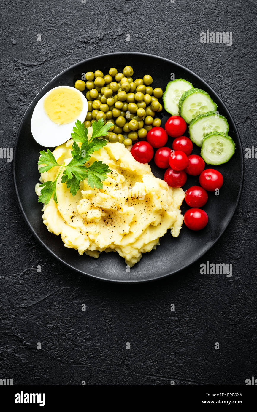 Kartoffelpüree mit grünen Erbsen, Tomaten und gekochtem Ei. Kartoffelschnee auf Platte mit Gemüse und Ei Stockfoto