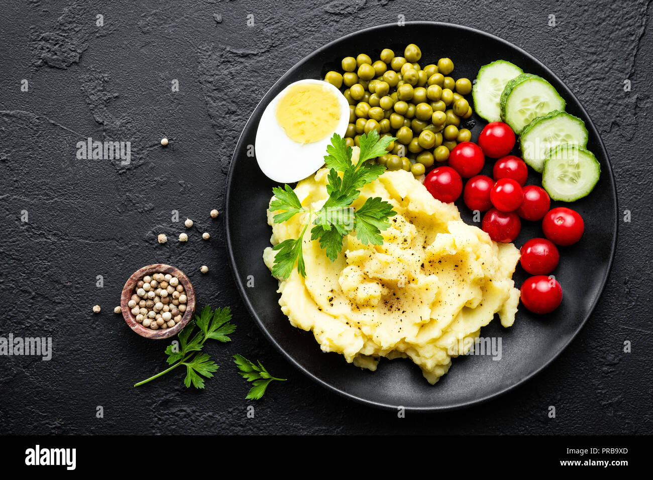 Kartoffelpüree mit grünen Erbsen, Tomaten und gekochtem Ei. Kartoffelschnee auf Platte mit Gemüse und Ei Stockfoto