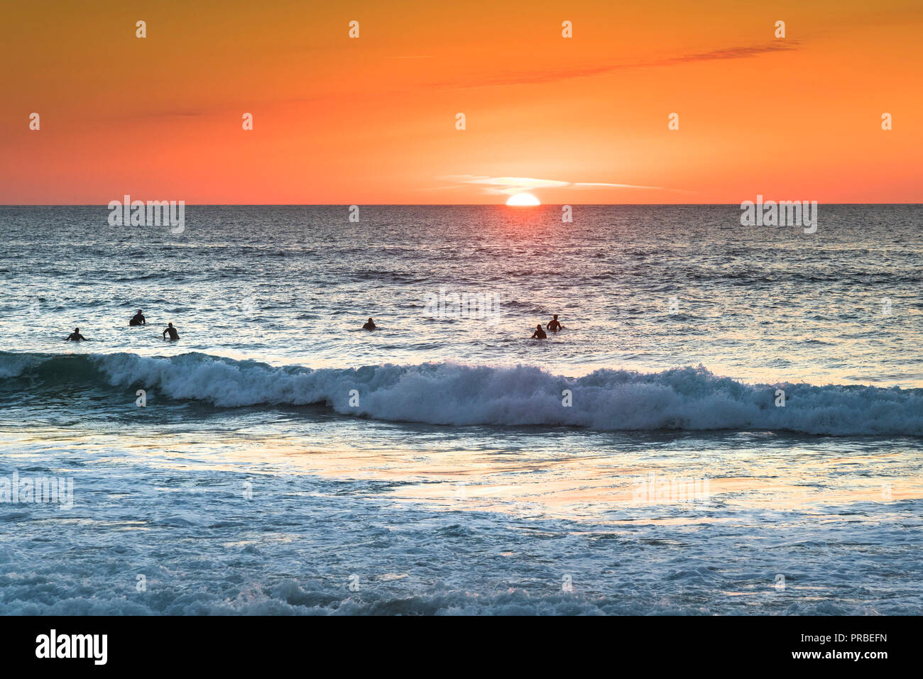 Surfer für eine Welle durch eine intensive Sonnenuntergang am Fistral Beach in Newquay in Cornwall silhouetted warten. Stockfoto