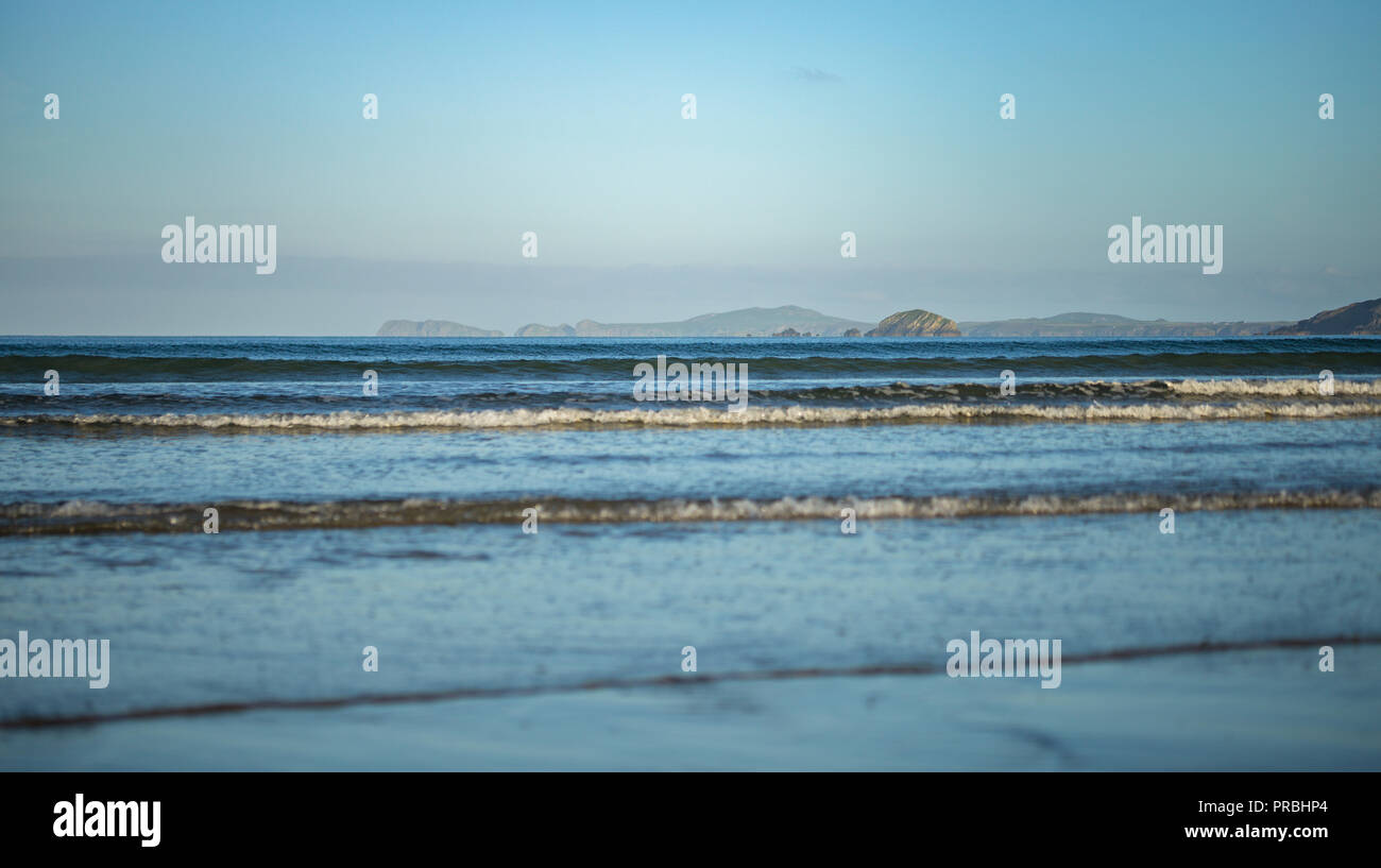 Lange blaue Wellen mit malerische felsige Küste im Hintergrund. Newgale in Pembrokeshire, Großbritannien Stockfoto