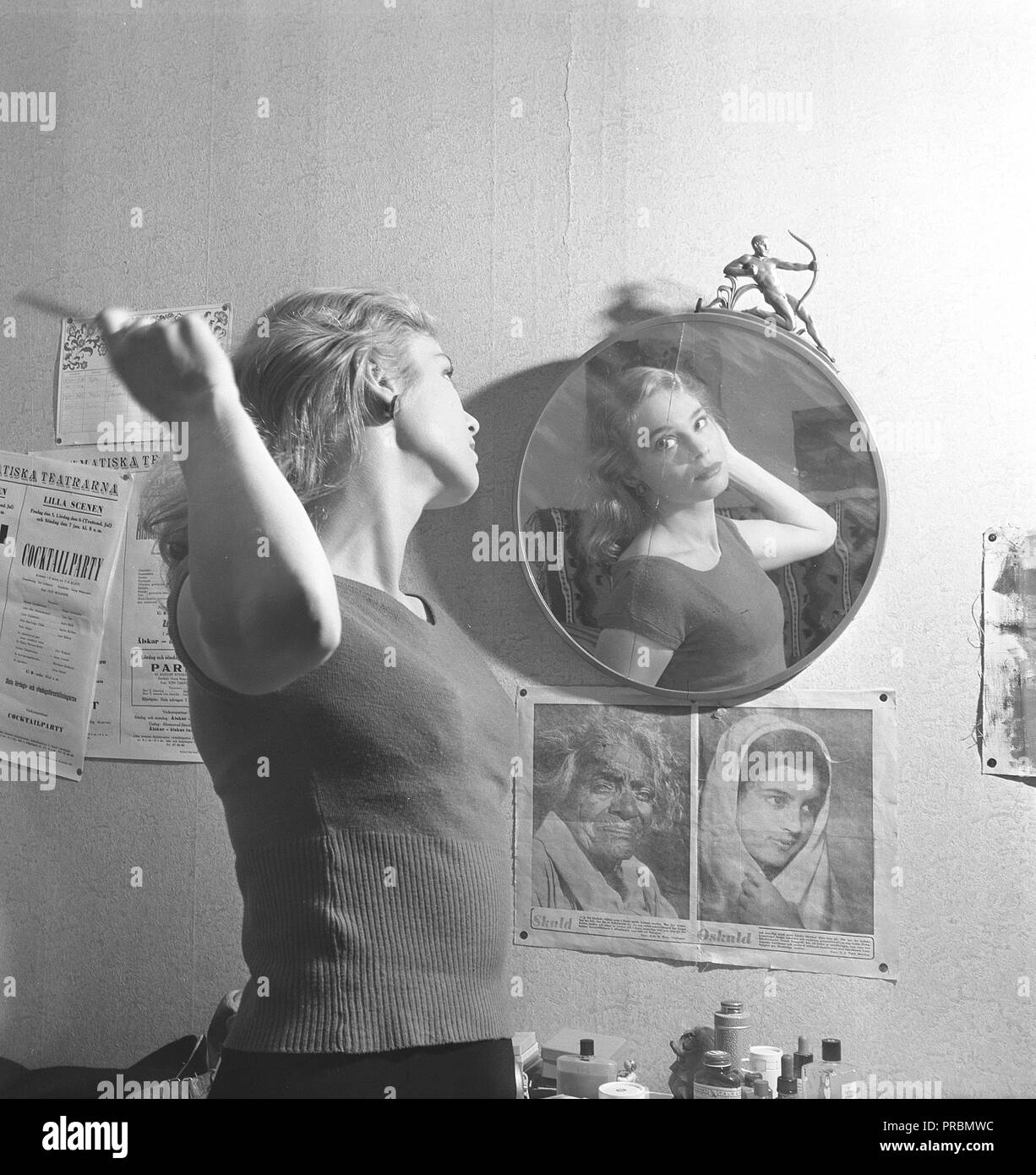 Frau in den 1950er. Eine junge Frau steht vor einem Spiegel und kämmt sich die Haare. Hier ist die schwedische Schauspielerin Ingrid Thulin abgebildet. 1926-2004. Beachten Sie, wie die Fotografin sie im Spiegel positioniert hat, sodass der Riss im Art déco-Spiegelglas durch ihr Gesicht geht. Schweden 1951. Kristoffersson Ref. BB39-12 Stockfoto