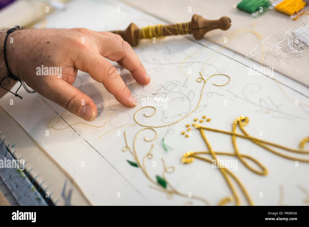 Detail der Hände eines Mannes Sticken mit einem Nähfaden auf. Einzelheiten der embroiderywith goldfarbene Gewinde Stockfoto