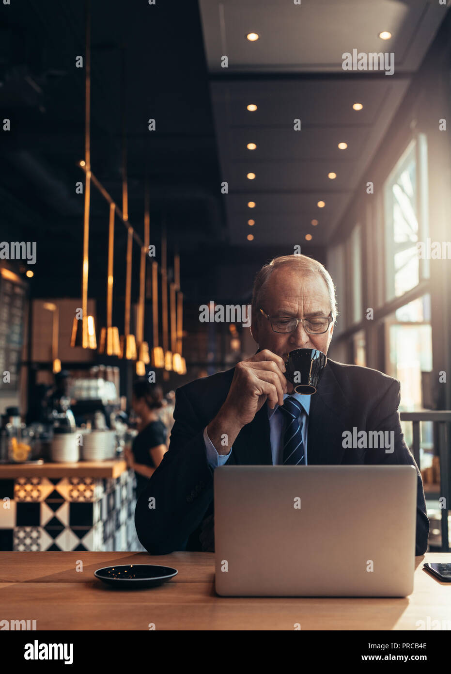 Vertikaler älterer Geschäftsmann am Laptop suchen und Kaffee im Cafe. Reifer Mann im Anzug im Cafe sitzen mit Laptop trinken Stockfoto