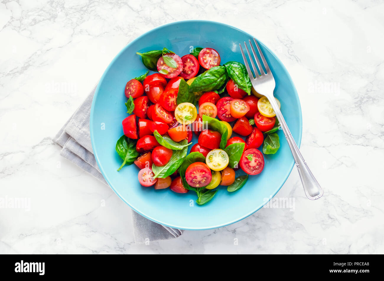 Hell Tomaten Salat von roten und gelben Tomaten cherry mit Basilikum, Olivenöl und Balsamico weißer Marmor Hintergrund. Vegetarische und vegane Stockfoto