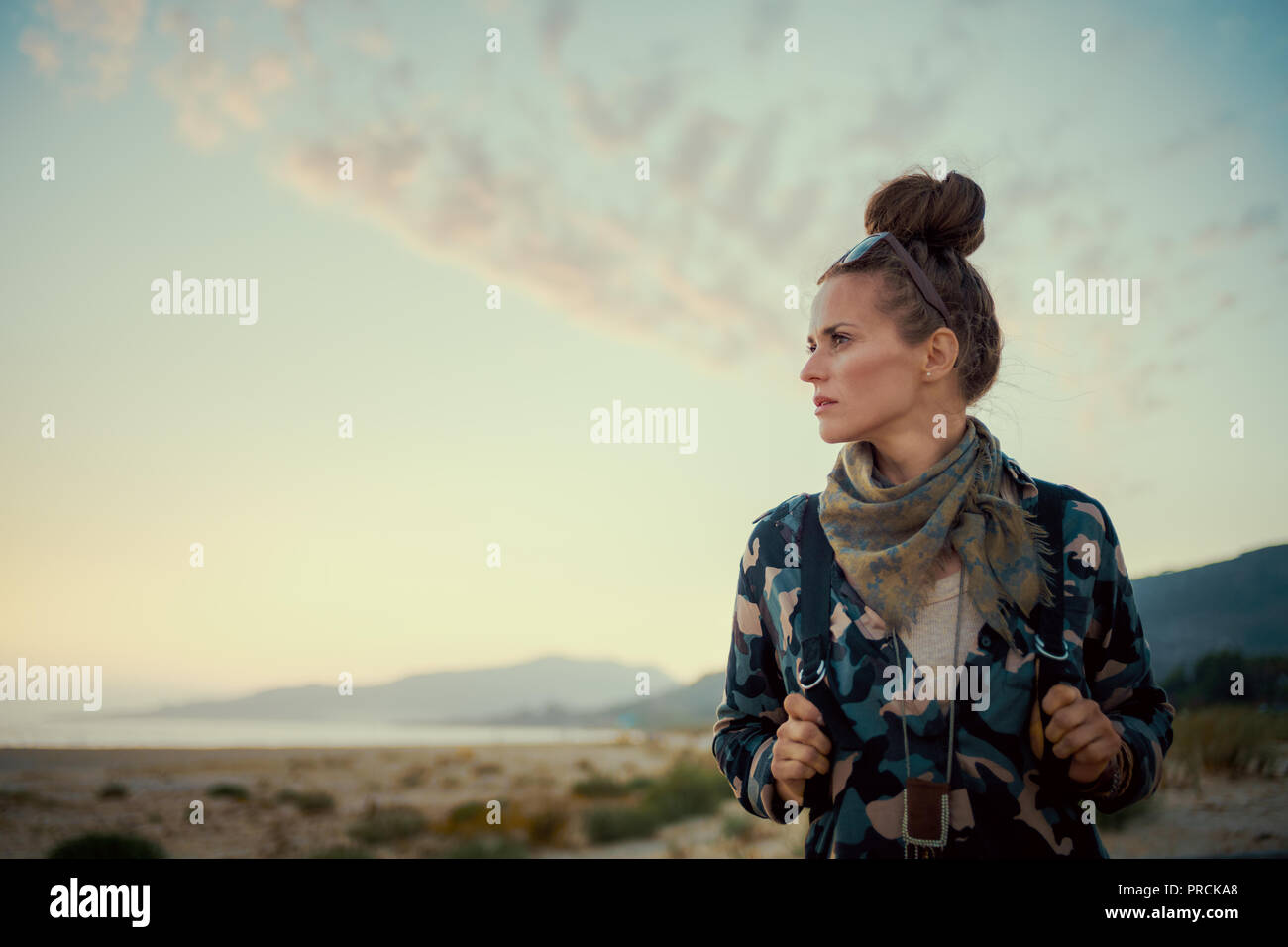 Junge Frau in Wanderausrüstung beiseite suchen gegen die Berge und das Meer Landschaft bei Sonnenuntergang Stockfoto